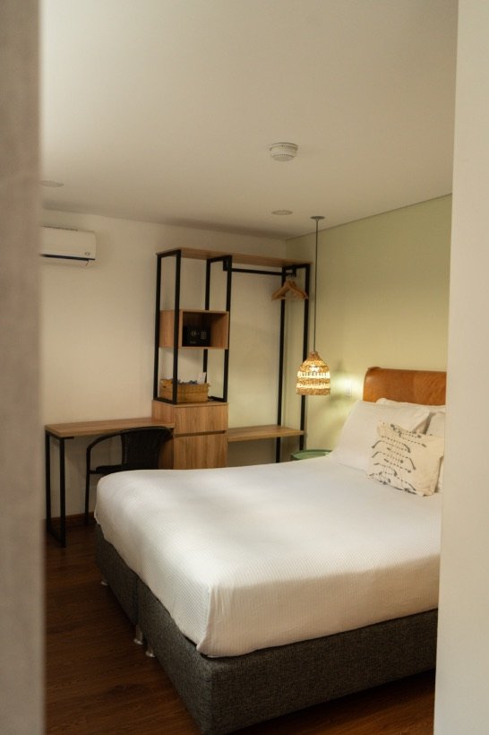 Standard Room with queen bed, leather headboard, desk and open wardrobe