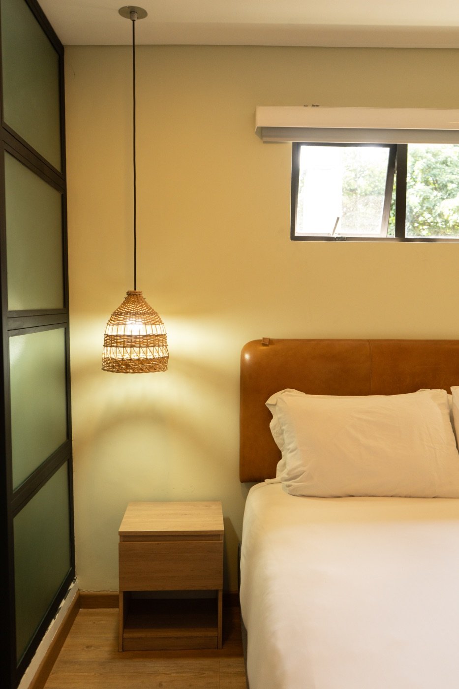 Bedside detail with rattan pendant lamp and leather headboard in the Standard Room